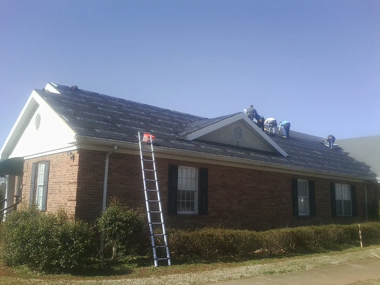 Crew tearing shingles off a brick ranch roof with a ladder set — Emergency Roof Repair work by our crew in Silver Lake
